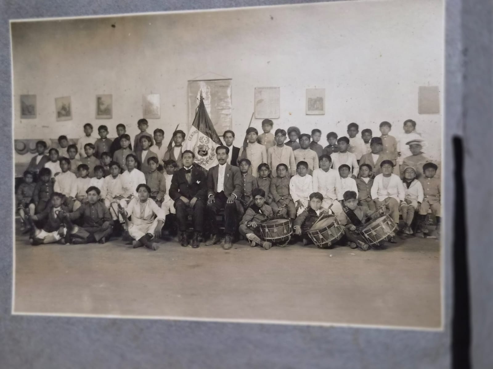 Grupo de niños, jóvenes y adultos reunidos en un centro escolar, con estandarte e instrumentos de percusión, en una fotografía histórica de la comunidad japonesa en el Perú.